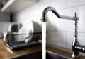 Water flowing out of a kitchen stainless steel tap into the sink. Wasting water by leaving a chrome faucet tap running. Overusing Royalty Free Stock Photo