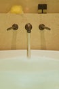 Water flowing out into white bathtub from brass tap mounted on the wall Royalty Free Stock Photo