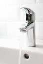 Water flowing from the tap into white ceramic sink and white tile wall, vertical. Detail modern bathroom