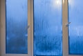 Water flows on the glass of the window in the winter in the evening in the apartment