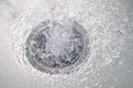 Water flows rapidly down a sink drain creating bubbles and splashes in a bright kitchen environment Royalty Free Stock Photo