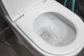 Water flushing in toilet bowl. White hanging toilet seat on white toilet in the home bathroom with grey tiles in Royalty Free Stock Photo