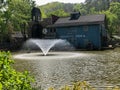 Water fountain in small pond by old grist mill building Royalty Free Stock Photo