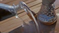 water from jug pouring into glass on wooden table outdoors. Royalty Free Stock Photo