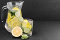 Water with lemon and cucumber and mint in a glass cup and in a jug next to half a fresh lemon and cucumber slices on a black backg Royalty Free Stock Photo