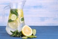 Water with lemon and cucumber and mint in a glass jug next to a fresh lemon on a blue and blue wooden background Royalty Free Stock Photo