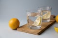 Water with lemon in two glasses on a wooden stand on a light blue background Royalty Free Stock Photo