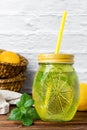 Water with mint in yellow glass, lemon in basket on wooden table