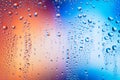 Water particles stagnant on the glass with two opposite reddish-blue colors. Blurred colorful background of droplets Royalty Free Stock Photo