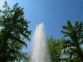 Water pillar with a splash from a drop against the background of blue sky and green trees, bottom view. Fountain creates a cascade Royalty Free Stock Photo