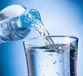 Water poured out of plastic bottle into glass isolated on blue background Royalty Free Stock Photo