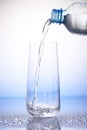 Water pouring from bottle into drinking glass on drops Royalty Free Stock Photo