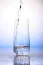 Water pouring into one-third full drinking glass on drops Royalty Free Stock Photo