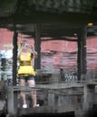 Water reflection of a woman in a yellow dress standing in a pavilion and taking a photo.