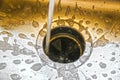 Water running into a garbage disposal of a stainless steel sink with gold toned blurred background and sharp silver foreground