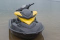 Water scooter boat with black deck and steering part and yellow streamlined vertical part standing near shore in shallow water