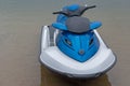 Water scooter boat with white deck, black steering part and blue streamlined vertical part standing in shallow water of lake. Royalty Free Stock Photo