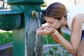 Water shortage emergency. Young woman hydrates herself from a fountain during a heat spike in the city