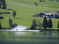 Water skier with a boat in front of an Alpine farm backdrop with a barn