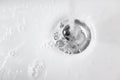 Water with soap foam in white ceramic sink drains down Royalty Free Stock Photo