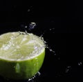 Water splashing over half a lime. Black background.