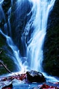 Water spray below small waterfall on mountain stream, water is falling over mossy boulder. The spray create on level and gravel mi Royalty Free Stock Photo