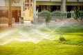 Water sprinkler spraying over green fresh grass lawn, flower bed in garden,backyard on hot summer day. Automatic Royalty Free Stock Photo