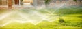 Water sprinkler spraying over green fresh grass lawn, flower bed in garden,backyard on hot summer day. Automatic Royalty Free Stock Photo