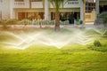 Water sprinkler spraying over green fresh grass lawn, flower bed in garden,backyard on hot summer day. Automatic watering Royalty Free Stock Photo