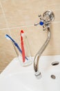 Water tap and glass with toothbrushes on a white ceramic wash basin Royalty Free Stock Photo