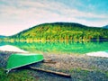 Watercolor effect. Abandoned fishing paddle boat on bank of Alps lake. Morning lake