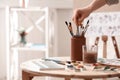 Watercolorist taking brush from holder on table in workshop