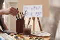 Watercolorist taking brush from holder on table in workshop