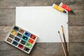 Watercolors with paint brushes and blank sheet of paper on wooden table Royalty Free Stock Photo