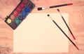 Watercolors, paintbrushes, paper, wooden desk