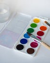 Watercolors of twelve colors in a box and brushes for painting, as well as a jar of water for painting on a white sheet Royalty Free Stock Photo