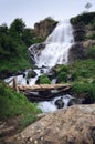 Waterfall with bridge, green forest and stones