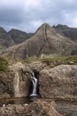 A waterfall cascades through rugged rocks at the Fairy Pools on Isle of Skye, set against the imposing Cuillin Mountains