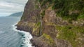 Waterfall falling into ocean from volcanic cliffs.