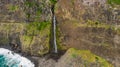 Waterfall falling into ocean from volcanic cliffs.