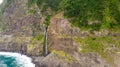 Waterfall falling into ocean from volcanic cliffs.