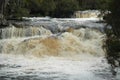 A waterfall in flood, with muddy water and white foam.