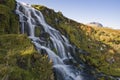 Waterfall flowing down hill with sky and mountains