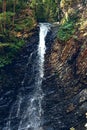 A waterfall flowing down from a Sheer cliffs . Blue clear water of mountain the river. Rocky stones and forest Alpine landscape Royalty Free Stock Photo