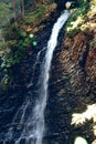 A waterfall flowing down from a Sheer cliffs . Blue clear water of mountain the river. Rocky stones and forest Alpine landscape Royalty Free Stock Photo