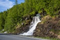 Waterfall flows from green forest just next to the asphalt road