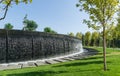 Waterfall flows in streams into granite bed of artificial river. Fountain in form of huge bowl. Public landscape city park