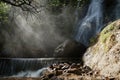 Waterfall and lower cascade in the forest with water fog lit with sunbeams Royalty Free Stock Photo