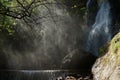 Waterfall and lower cascade in the forest with water fog lit with sunbeams Royalty Free Stock Photo