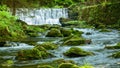 Waterfall in a mountainous rapid river with stones overgrown with moss